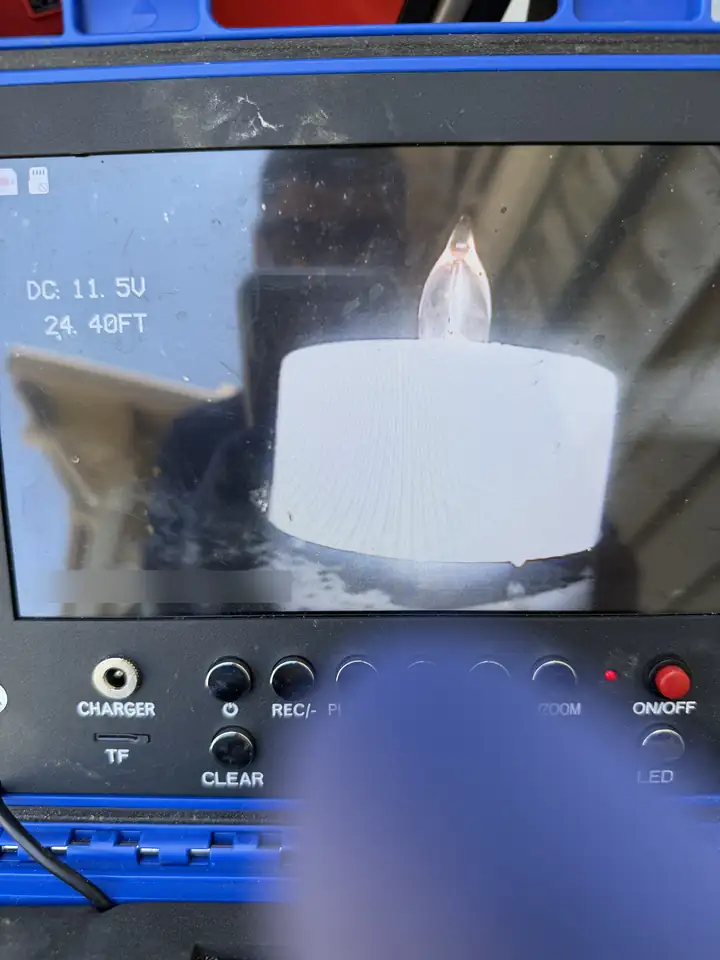 Sewer camera monitor showing a lit plastic candle inside a drain line, 24.40 FT on the screen, McKinney