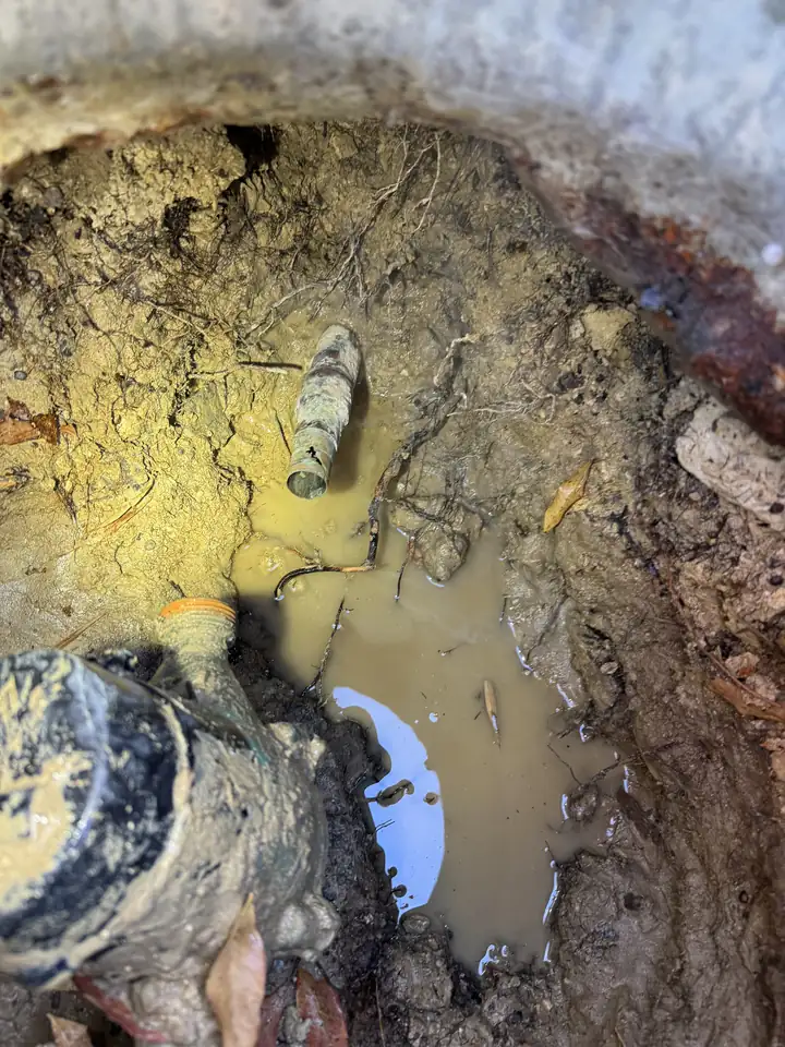 Muddy dig beside a water meter box with water standing in it and a pipe at the bottom, McKinney