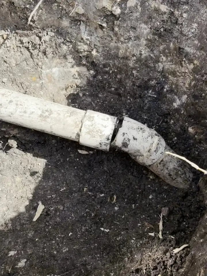 White PVC drain pipe separated at a joint in an open yard dig, Plano