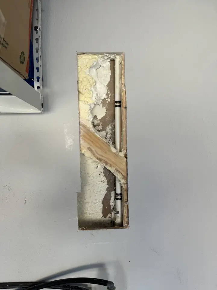 Opened garage drywall showing a water pipe in foam insulation where a nail went through it, Frisco