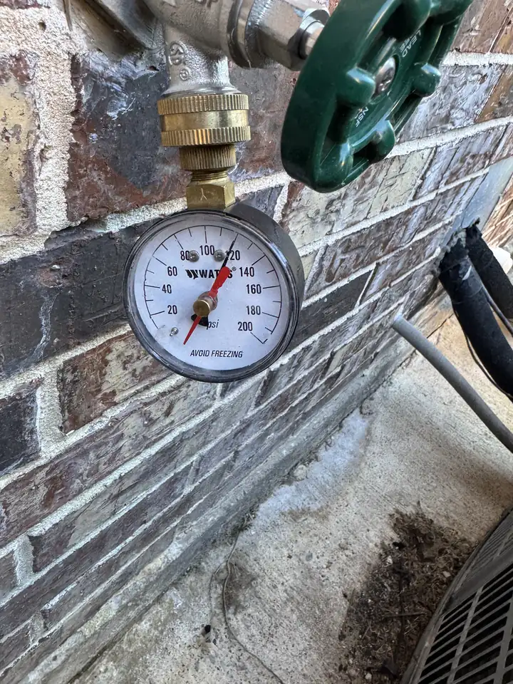 Water pressure gauge reading about 120 PSI on an outside spigot at a brick wall, Prosper