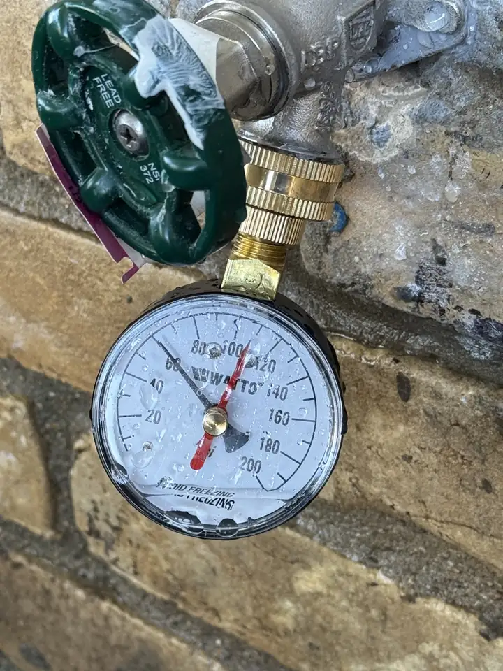 Pressure gauge on a new brass hose bib with a green handle at a brick wall, the black needle at 60 PSI, Allen