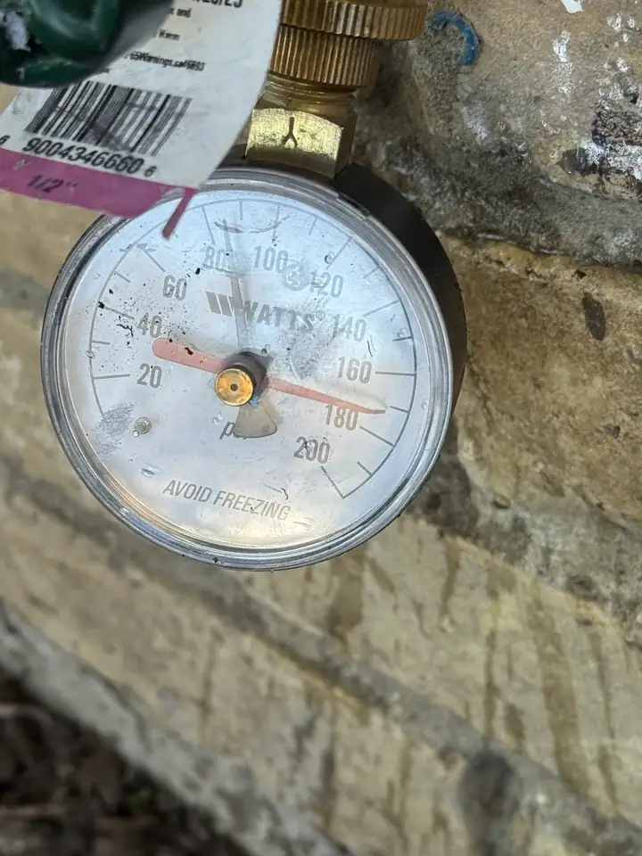 Watts pressure gauge on an outside faucet at a brick wall, the black needle near 90 PSI, Allen