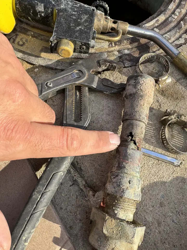 Finger pointing at a corrosion hole in a cut out piece of copper water line, tools beside it, McKinney