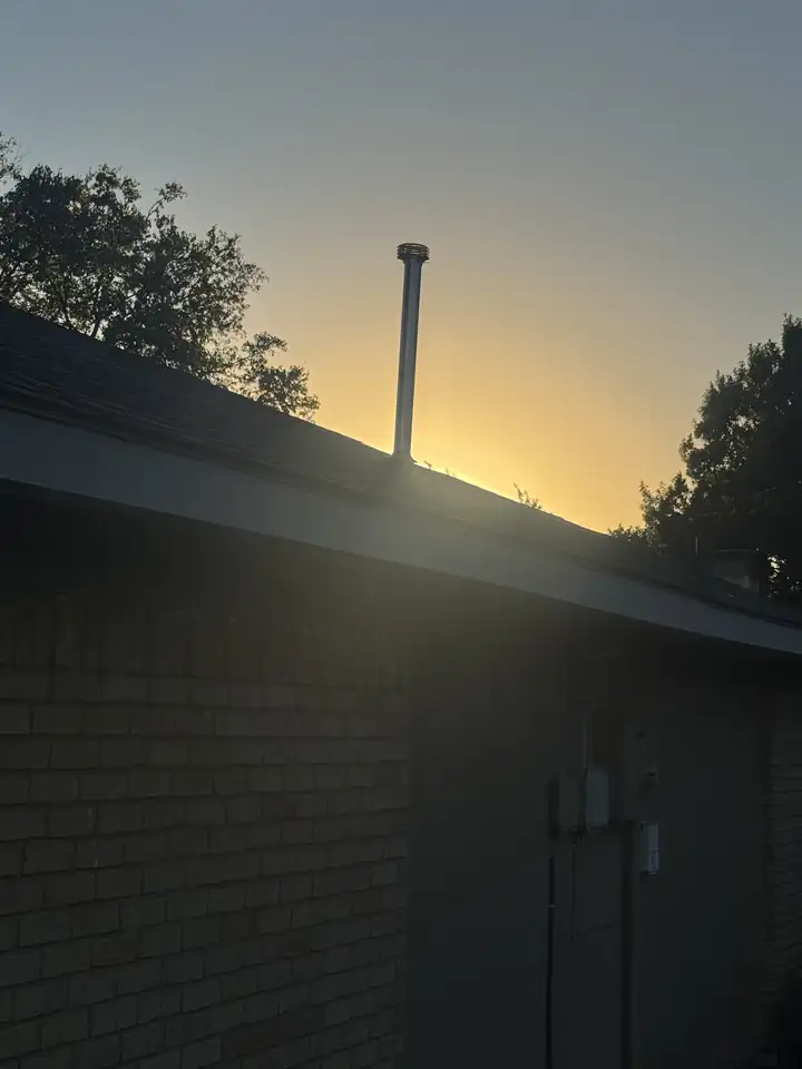 New double wall vent pipe with its cap above a roof line, brick wall and meter box below, sunset, Allen