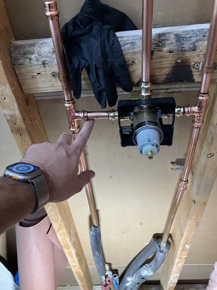 New shower valve pressed onto new copper risers inside an open stud wall, a hand pointing at it, McKinney