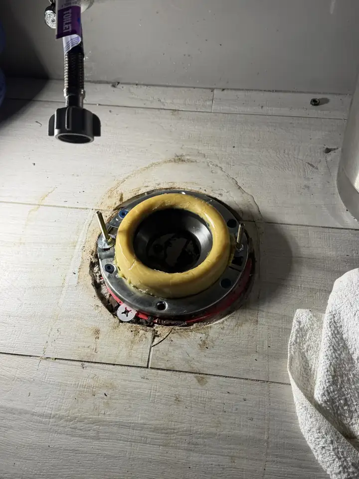 New steel flange ring with a fresh wax ring and bolts on a tile floor, the toilet supply line above, Allen