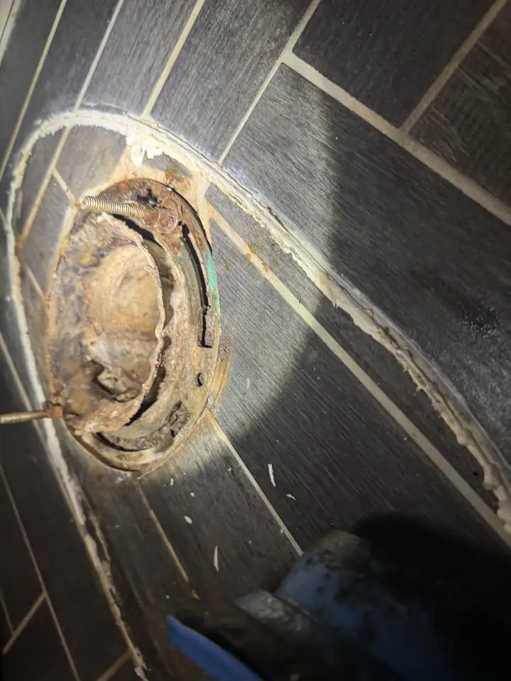 Old rusted and cracked toilet flange in a tile floor, Plano