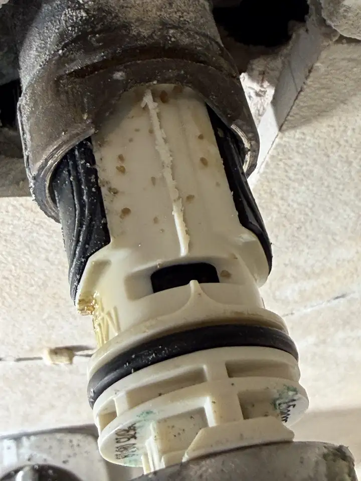 Shower valve cartridge covered in white calcium scale after removal, Frisco