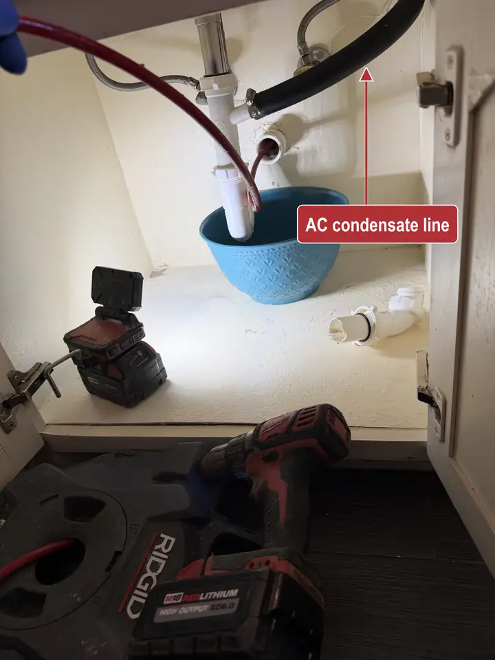 Sink drain line under a cabinet with the P-trap removed, a drain cable in the pipe and the black AC condensate line marked where it ties into the drain, Frisco