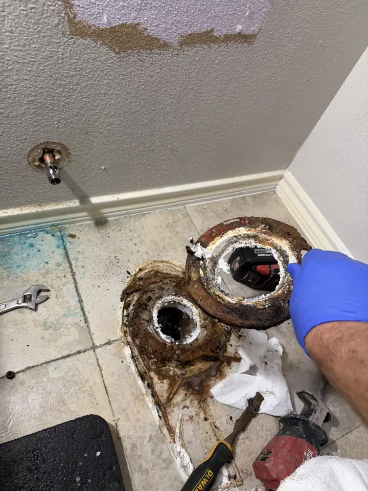 Rusted toilet flange on a tile floor with the toilet removed, a new flange ring and tools beside it, McKinney