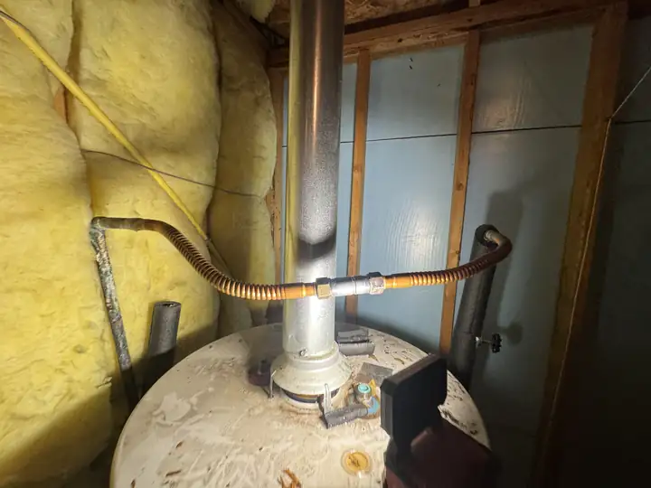 Top of a water heater in an attic with a flexible copper line joining the two supply pipes across it, the flue in the middle, Frisco